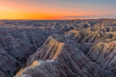 Panoramic view of the deeply eroded rocky pinnacles and layered geologic formations of the Badlands Wall at sunrise in Badlands National Park, South Dakota.